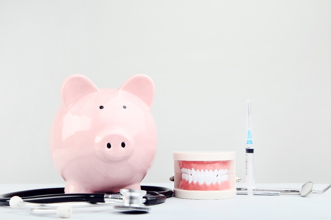 Pink piggy bank with stethoscope and teeth model on grey background