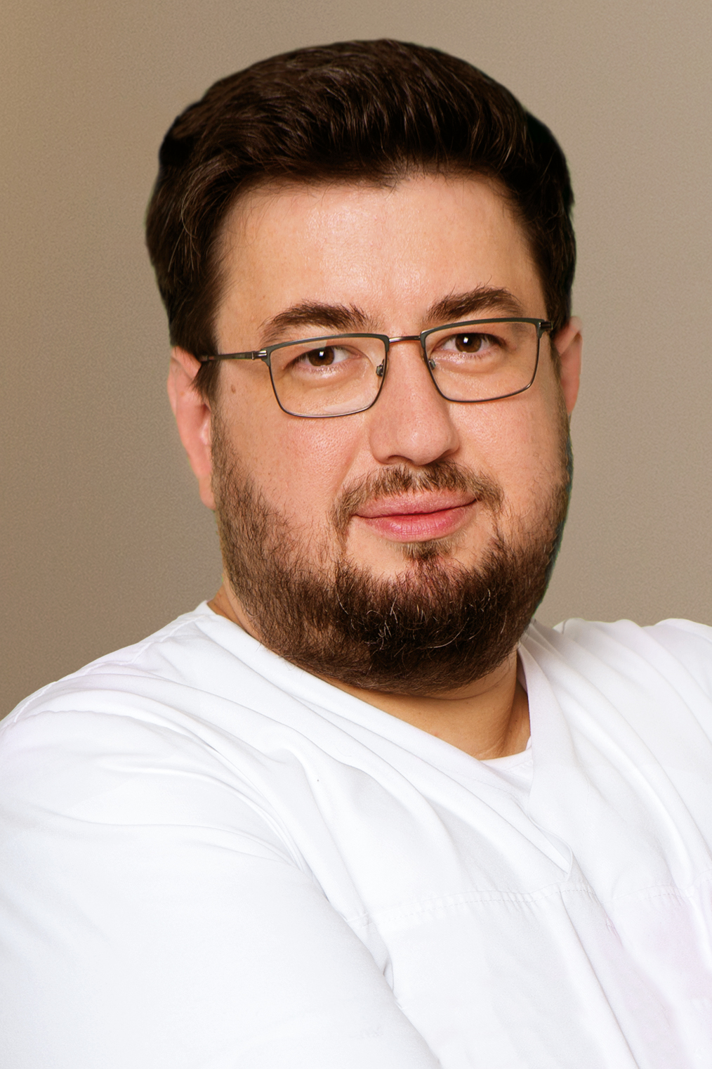 Ein Mann mit braunen Haaren und Bart lächelt leicht und trägt eine weiße Kleidung