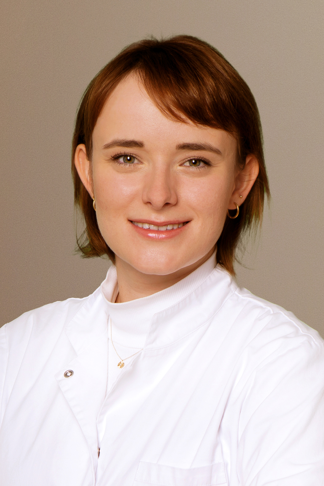 Junge Frau mit kurzem braunem Haar lacht freundlich in weißem Kittel