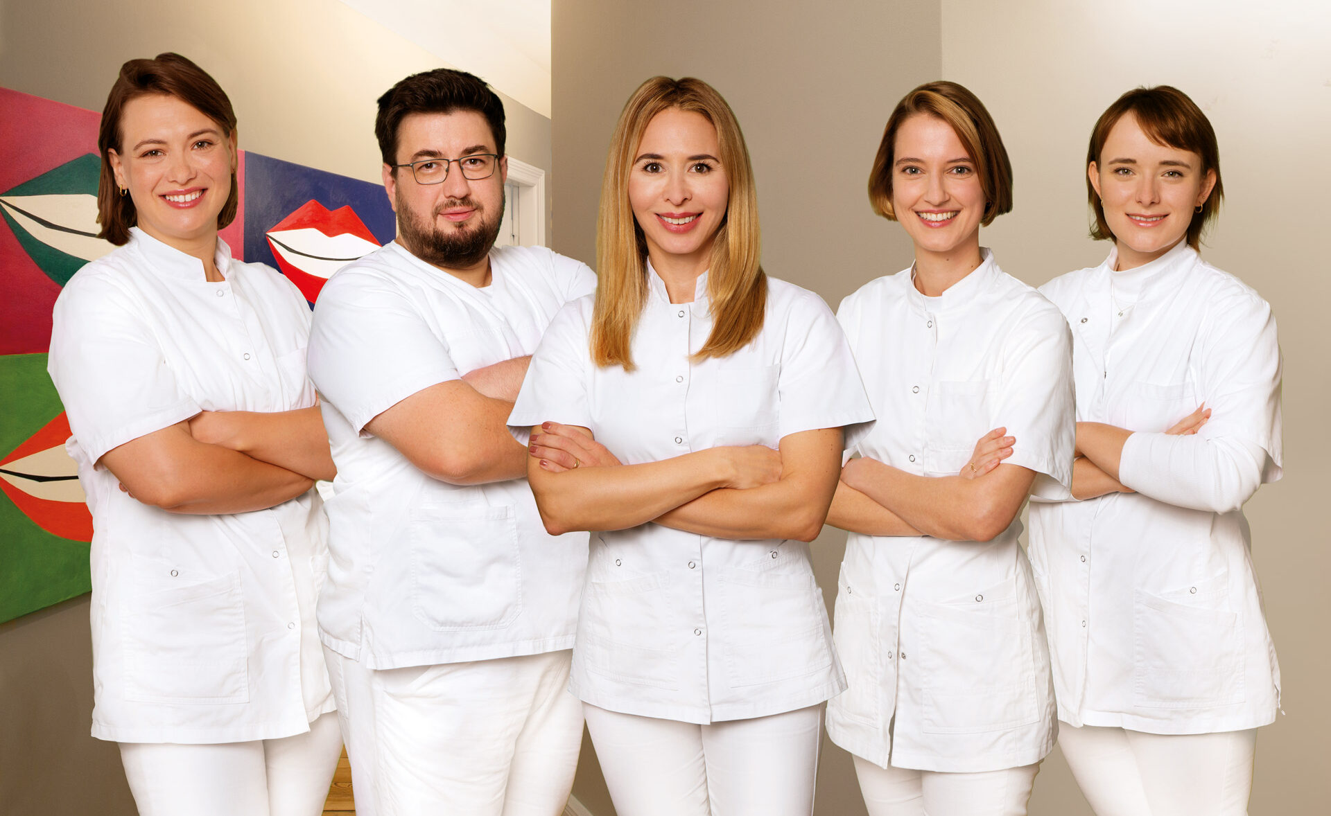 Fünf Zahnärztinnen und ein Zahnarzt in weißen Kitteln lächeln freundlich im Flur