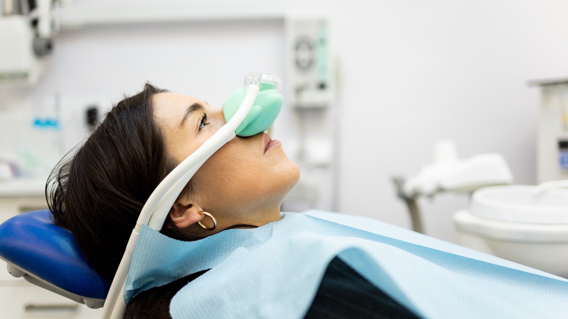 Eine erwachsene Frau sitzt in einer Zahnarztpraxis und trägt eine Nasenmaske, um Lachgas zu inhalieren.